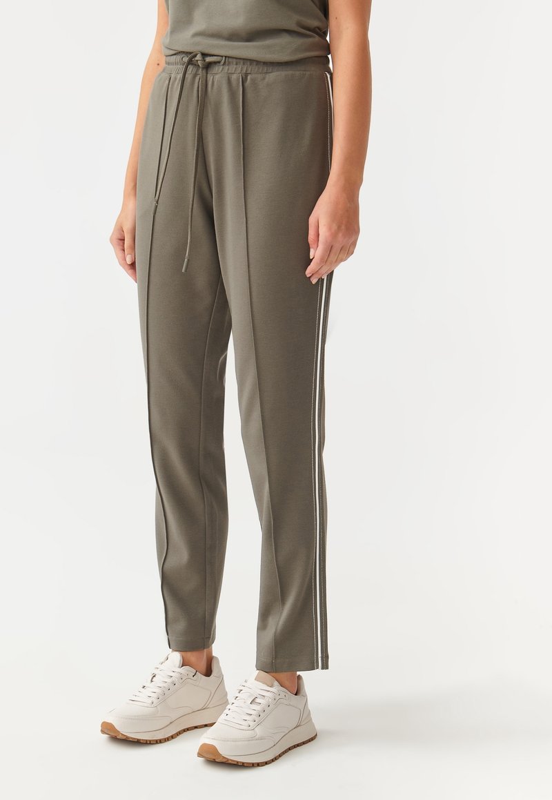 Olijfgroene joggers met een elastische tailleband, zijstrepen en een relaxte pasvorm. Gepaard met witte sneakers met een tan kleurige zool.