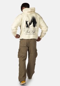 Felpa crema con una grafica nera sul retro, che presenta "CRYSTALPARK Nordic Nights." Abbinata a pantaloni cargo khaki e sneakers bianche.
