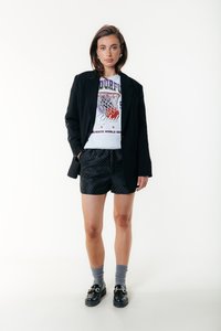 Črn blazer preko sive majice z barvitim motivom, kombiniran s črnimi kratkimi hlačami z belimi pikami, sivimi nogavicami in črnimi loaferji.