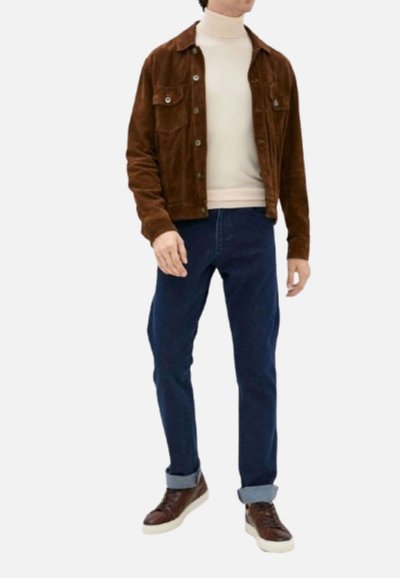 Giacca di velluto a coste marrone, dolcevita beige, jeans blu e sneaker marroni. La giacca presenta due tasche frontali. Materiale testa di moro su tutta la superficie.