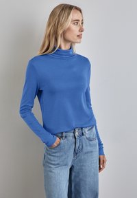 Blå långärmad polotröja i slät tyg, kombinerad med högmidjade ljusblå jeans som har en avslappnad passform och är instoppade.