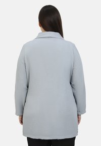Giacca lunga di tessuto blu chiaro, stropicciato, con colletto, maniche lunghe e taglio dritto, che arriva a metà coscia. Nessun hardware o motivo visibile.