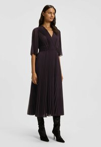 Syvän liilanvärinen plissé-mekko, jossa on V-kaula-aukko, lyhyet hihat ja teksturoitu vyötärön yksityiskohta. Yhdistetty tyylikkäisiin mokkanahkaisisiin korkokenkiin.