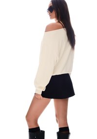 Krema barve off-shoulder pulover, črna mini krila, črne visokotlačne škornje. Gladka tekstura, sproščen kroj, dolgi rokavi, minimalni dodatki.