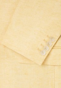 Chaqueta de traje de lino amarillo claro con una textura de patrón tejido y un conjunto de cuatro botones claros en el puño.