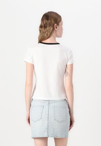Bela majica s kratkimi rokavi z črnimi ovratnikom, ki je kombinirana s svetlo modrim jeans krilom z ponavljajočim se logotipom in zadnjimi žepi.