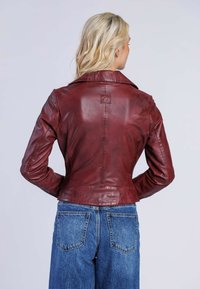 Burgunderläderjacka med en strukturerad design, spetsig krage och präglad logotyp på ryggen. Matchas med ljusblå vida jeans.