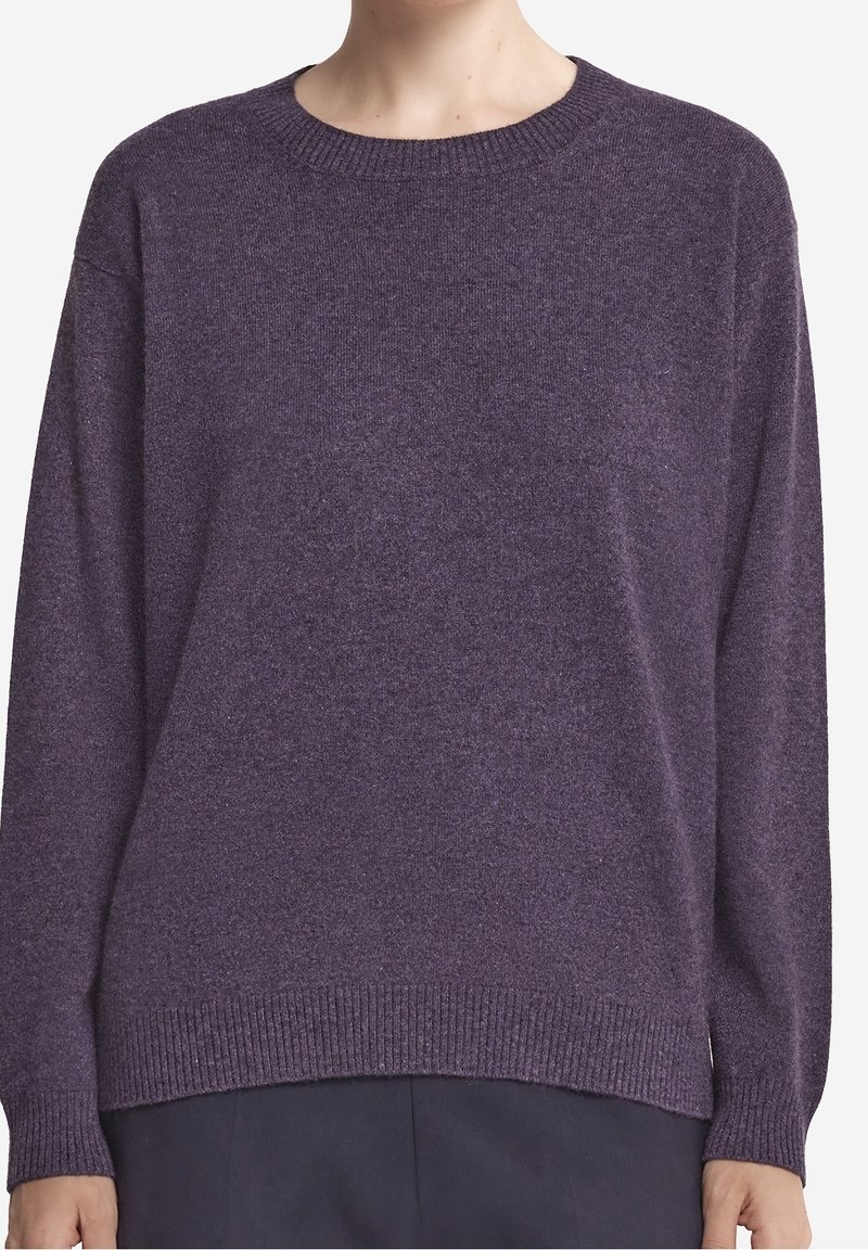 Personne portant un pull en maille violet à manches longues avec une encolure ronde et des poignets et un bas côtelés, associé à un pantalon sombre.