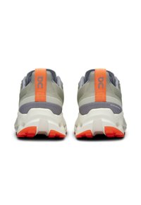 Grijze en beige sport schoenen met oranje accenten en een gestructureerde achterkant. Voorzien van een dikke zool en zichtbare dempings elementen.