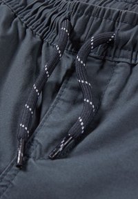 Gros plan sur une ceinture élastique noire avec un cordon noir et blanc sur un pantalon ou short en tissu sombre.