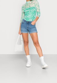 Top de manga larga con patrón en espiral verde menta, combinado con pantalones cortos de mezclilla y botas blancas gruesas con cordones. Los accesorios incluyen una pequeña bolsa blanca.