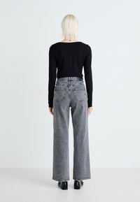 Top negro de manga larga combinado con jeans grises de tiro alto y pierna ancha, que presentan detalles de tachuelas en el dobladillo y los bolsillos.