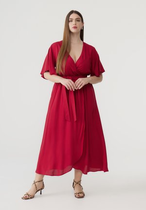 Abito midi rosso fluente con maniche a farfalla, scollo a V e cintura legata in vita. Il modello indossa sandali con tacco in stampa leopardata.