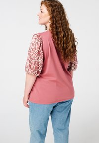 Roze T-shirt met geborduurde pofmouwen in crèmekleurig bloemenontwerp, gecombineerd met lichtblauwe denim broek. Glad materiaal, losse fit.