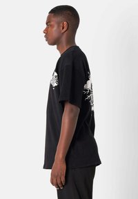 Camiseta negra de algodón con un diseño gráfico en la parte posterior, mangas cortas y un corte relajado. Sin patrones visibles ni herrajes.