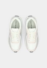 Un paio di sneakers bianche Calvin Klein con dettagli beige chiaro e lacci bianchi, viste dall'alto su uno sfondo semplice.