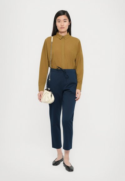 Gorčična srajca z dolgimi rokavi, mornarsko modri hlače z vrvico, črne balerinke in kremasta torbica s verigo. Enostaven, prilagojen dizajn.