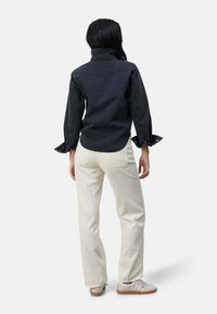 Donkerdenim overhemd met een hoge kraag en opgerolde mouwen, gecombineerd met crèmekleurige corduroy broek. De broek heeft een gestructureerd ribbelpatroon.