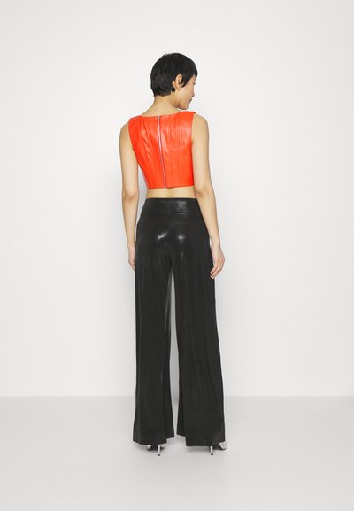 Top corto rojo con una textura suave y cremallera en la parte posterior, combinado con pantalones anchos brillantes negros de cintura alta para una silueta ajustada.