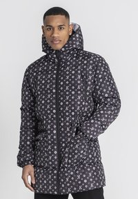 Chaqueta de plumas negra con un patrón de logo repetido, cierre de cremallera, capucha ajustable y bolsillos laterales. Textura suave con un acabado brillante.