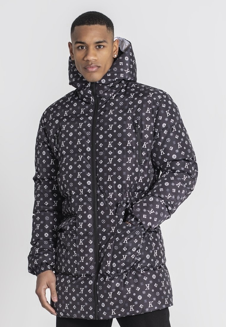 Chaqueta de plumas negra con un patrón de logo repetido, cierre de cremallera, capucha ajustable y bolsillos laterales. Textura suave con un acabado brillante.