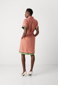 Kleid mit kurzen Ärmeln in Orange mit einem gemusterten Design, grünem Saum und einem Taillengürtel. Verfügt über schwarz-weiße Akzente am Saum.