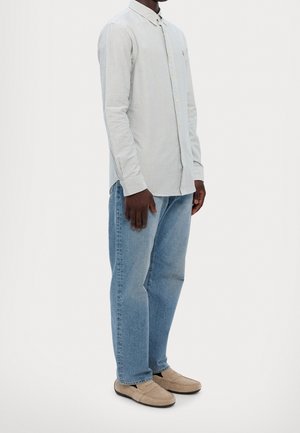 Camisa de rayas azul claro de manga larga con cuello abotonado, usada con jeans azul claro y zapatos tipo slip-on beige.
