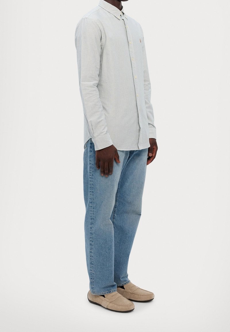 Camicia a righe azzurro chiaro con maniche lunghe e colletto a bottone, abbinata a jeans azzurro chiaro e scarpe slip-on beige.