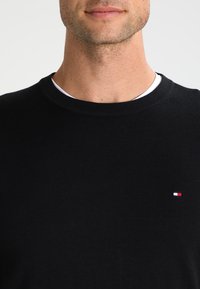 Maglione a girocollo nero in maglia con vestibilità regolare. Presenta un piccolo logo rosso, bianco e blu sul petto. Texture liscia.