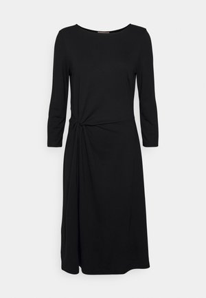 Robe noire en tissu lisse, à manches longues, avec un décolleté rond, un détail de taille nouée et une silhouette fluide.
