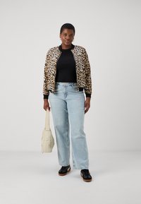 Leopard-print bomber jacket with ribbed cuffs, black top, light blue jeans, and black sneakers; holding a cream-colored bag.