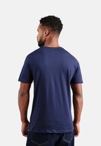 Camiseta de algodón azul marino, de mangas cortas, cuello redondo, con una textura suave y un diseño sencillo. La vista desde la parte posterior muestra un corte relajado.