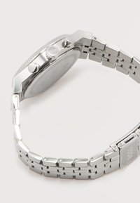 Ασημένιο μεταλλικό ρολόι χειρός με συνδεδεμένο βραχιόλι, πλαϊνή όψη που δείχνει δύο κουμπιά πίεσης και κορώνα με χάραξη "BOSS".