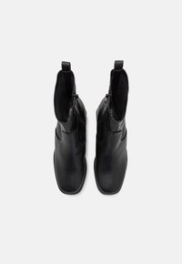 Juodos odinės kulkšninių botų su elegantišku dizainu, smailiu batu, šonine užtrauktuko uždarymo sistema ir vilkimo kilpomis. Lygus paviršius su minimaliu siuvimo detalių kiekiu.