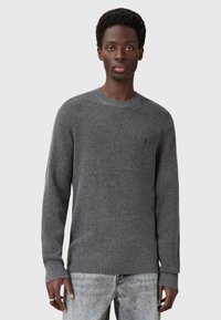 Szary, strukturalny sweter z dzianiny o okrągłym dekolcie i długich rękawach. Posiada małe logo na klatce piersiowej. Połączony z jasnoszarymi dżinsami.