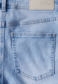 Ljust blå denimjeans med en enda bakficka, med synlig sömnad och en läderetikett vid midjan med varumärkestext.