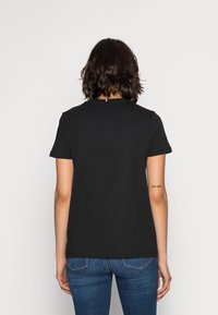 Black cotton t-shirt with short sleeves, round neckline, and straight cut. Features a small colored tag at the back neck. Paired with blue jeans.