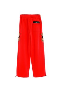Pantalones de chándal rojos con cinturilla elástica y un bolsillo lateral. Con detalles de osos bordados en negro y beige a cada lado. Textura suave.