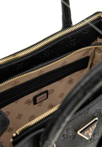 Sac à main en simili cuir noir avec des détails en or, fermeture à glissière, et un intérieur beige avec un motif de logo répétitif et une poche zippée.