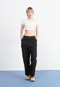 T-shirt blanc court, pantalon noir taille haute avec un bouton, et chaussures beige. Design simple et épuré avec une palette de couleurs neutres.