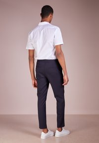 Krátký rukáv bílá košile s knoflíkovým límcem, kombinovaná s námořnickými zúženými kalhotami a bílými teniskami, s hladkou texturou a elastickým pasem.