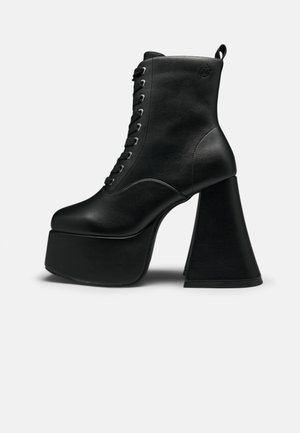 Stivaletto nero con plateau, allacciatura frontale e tacco largo a blocco, texture in pelle liscia e cinturino posteriore.