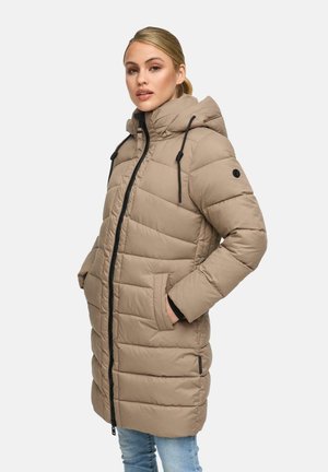 Jeune femme aux cheveux blonds portant un manteau long matelassé beige avec capuche et fermeture éclair noire, les mains dans les poches, contre un fond uni.