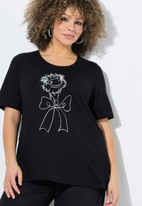 Camiseta de algodón negra con una ilustración de estilo caricaturesco en blanco de un personaje con un lazo, de manga corta y un corte holgado.