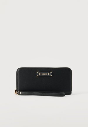 Petit porte-monnaie Guess noir avec plaque de logo dorée et fermeture éclair, présenté sur un fond clair uni.