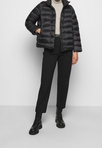 Sort pufferjakke med høj krave, præget af vandret syninger. Båret over en lys grå top og parret med sorte bukser og snørebåndsstøvler.