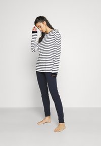 Cămașă cu dungi, cu mânecă lungă, în alb și bleumarin, cu o croială relaxată, asociată cu colanți bleumarin. Material din bumbac; design casual, cu manșete striate.