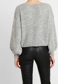 Grå virkade tröja med lös passform, ribbad struktur och ballongsärmar, kombinerad med svarta tajta byxor, som visar en rundad halsringning.
