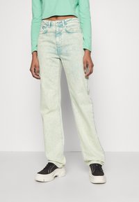 Light green high-waisted jeans with a faded wash, straight-leg design, and contrasting stitching details. Model paired with black sneakers.