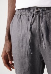 Gray linen trousers featuring an elastic waistband with a drawstring and side pockets. The fabric appears soft with a natural texture.